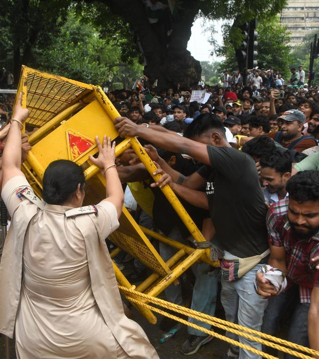 Demonstrierende stehen neben einem beschädigten Polizeibus nach Ausschreitungen bei einer Protestkundgebung in Neu-Delhi.