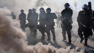 09.06.2025, USA, Los Angeles: Die Polizei ist durch Rauch auf dem 101 Freeway in der Nähe des Metropolitan Detention Center in der Innenstadt von Los Angeles zu sehen.