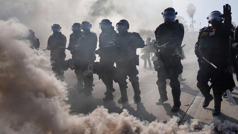 09.06.2025, USA, Los Angeles: Die Polizei ist durch Rauch auf dem 101 Freeway in der Nähe des Metropolitan Detention Center in der Innenstadt von Los Angeles zu sehen.
