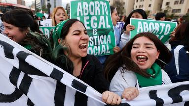 Zwei junge Frauen halten ein Banner nach oben und rufen.