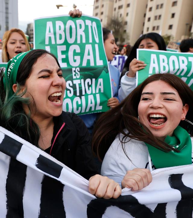 Zwei junge Frauen halten ein Banner nach oben und rufen.