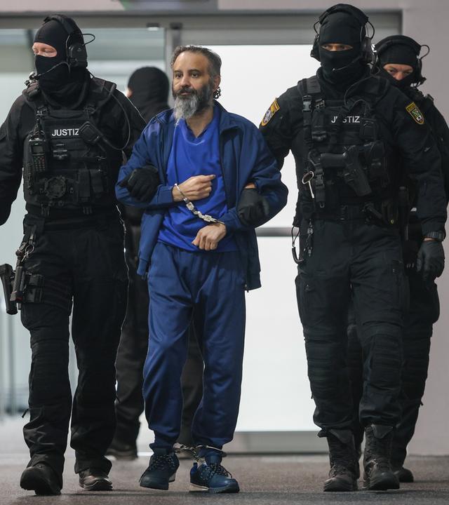  Justizbeamte führen den Angeklagten Taleb al-Abdulmohsen in den Gerichtssaal des temporären Gerichtsgebäudes vom Landgericht Magdeburg. 