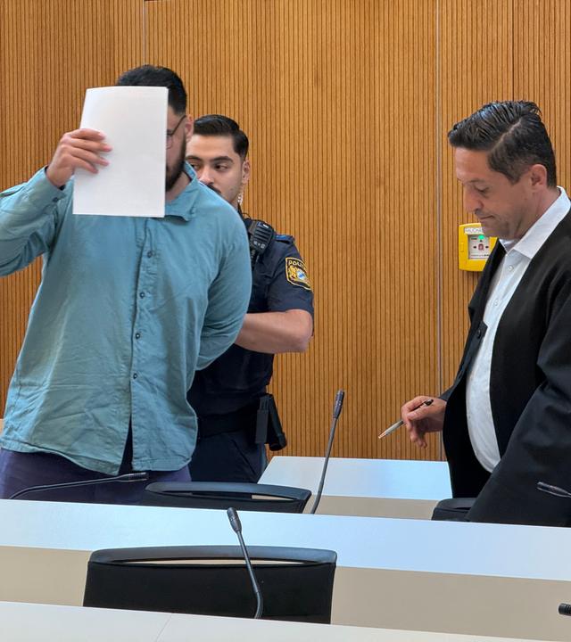 Der Angeklagte Farhad N. (M) steht neben seinem  Anwalt Ömer Sahinci (r) und Justizibeamten im Prozesssaal an seinem Platz. 