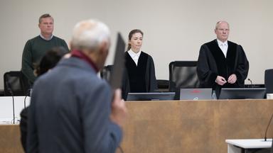 Der Angeklagte (vorne) steht vor der Verkündung des Urteils im Prozess gegen den Ex-Stasi-Mitarbeiter wegen Mordes vor dem Landgericht und verdeckt sein Gesicht.
