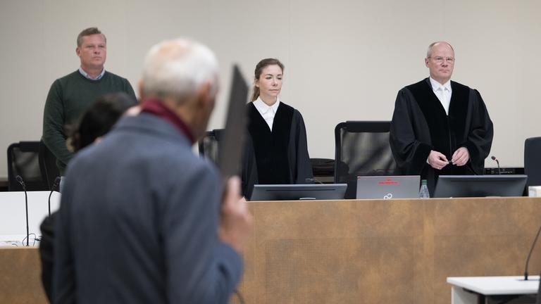 Der Angeklagte (vorne) steht vor der Verkündung des Urteils im Prozess gegen den Ex-Stasi-Mitarbeiter wegen Mordes vor dem Landgericht und verdeckt sein Gesicht.