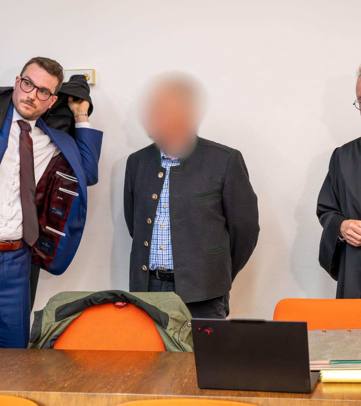 Ein beschuldigter Bahnmitarbeiter (M) steht vor Prozessbeginn um das tödliches Zugunglück in Garmisch-Partenkirchen vom 3. Juni 2022 zwischen seinen Anwälten im Gerichtssaal des Landgericht München II.