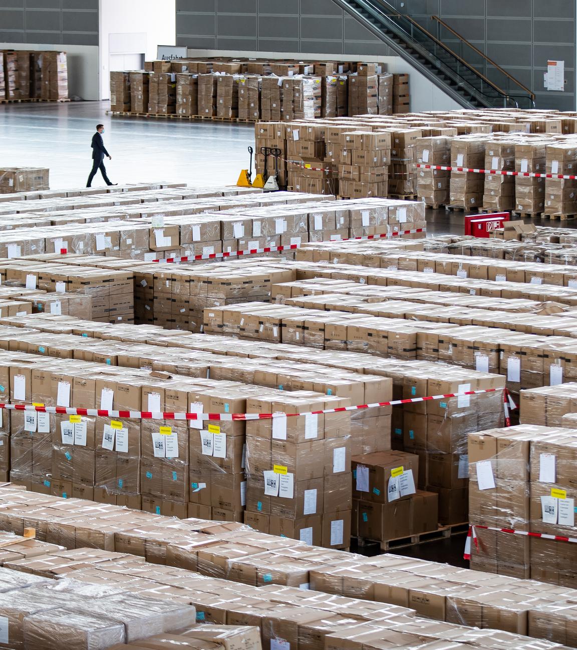 Ein Mann mit Schutzmaske geht an zahlreichen Kartons mit Schutzausrüstung in Millionenzahl vorbei.