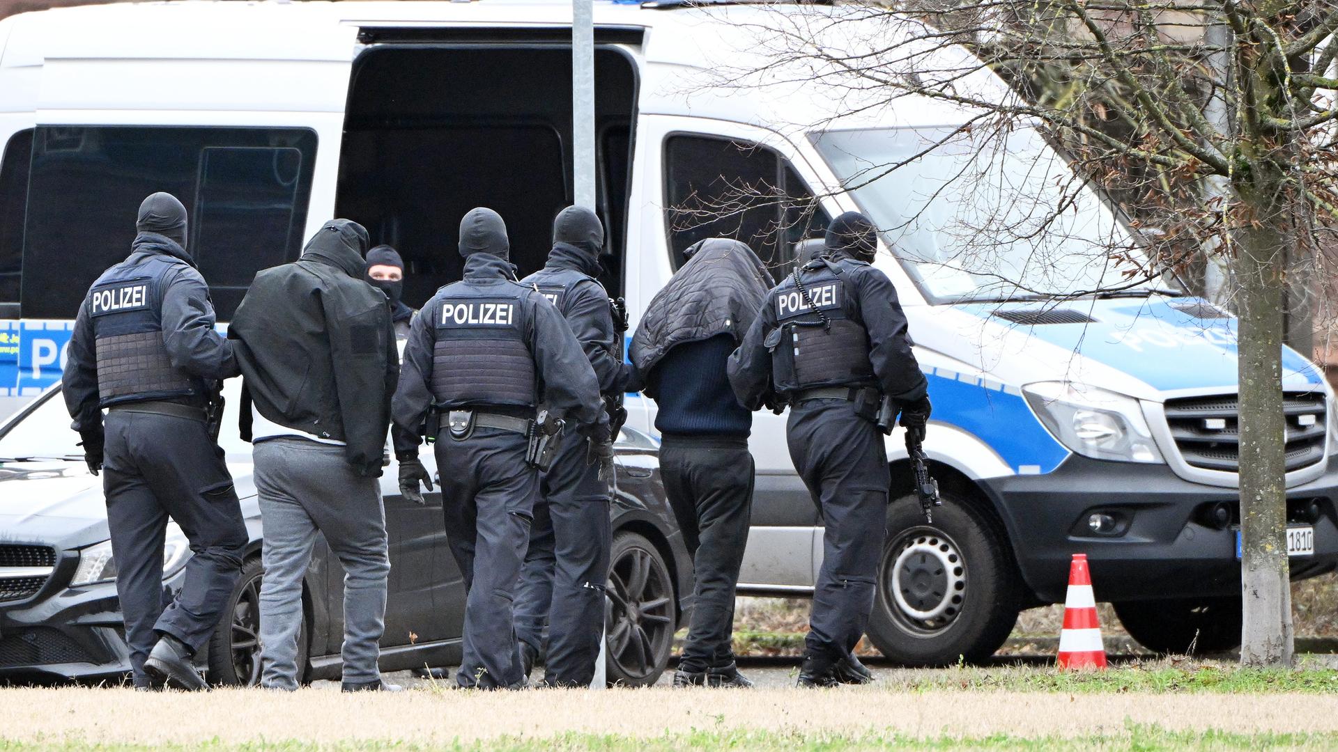 Baden-Württemberg, Karlsruhe: Zwei Personen werden von Polizisten bei einem Hubschrauberlandeplatz von einem Hubschrauber zu einem Auto geführt.