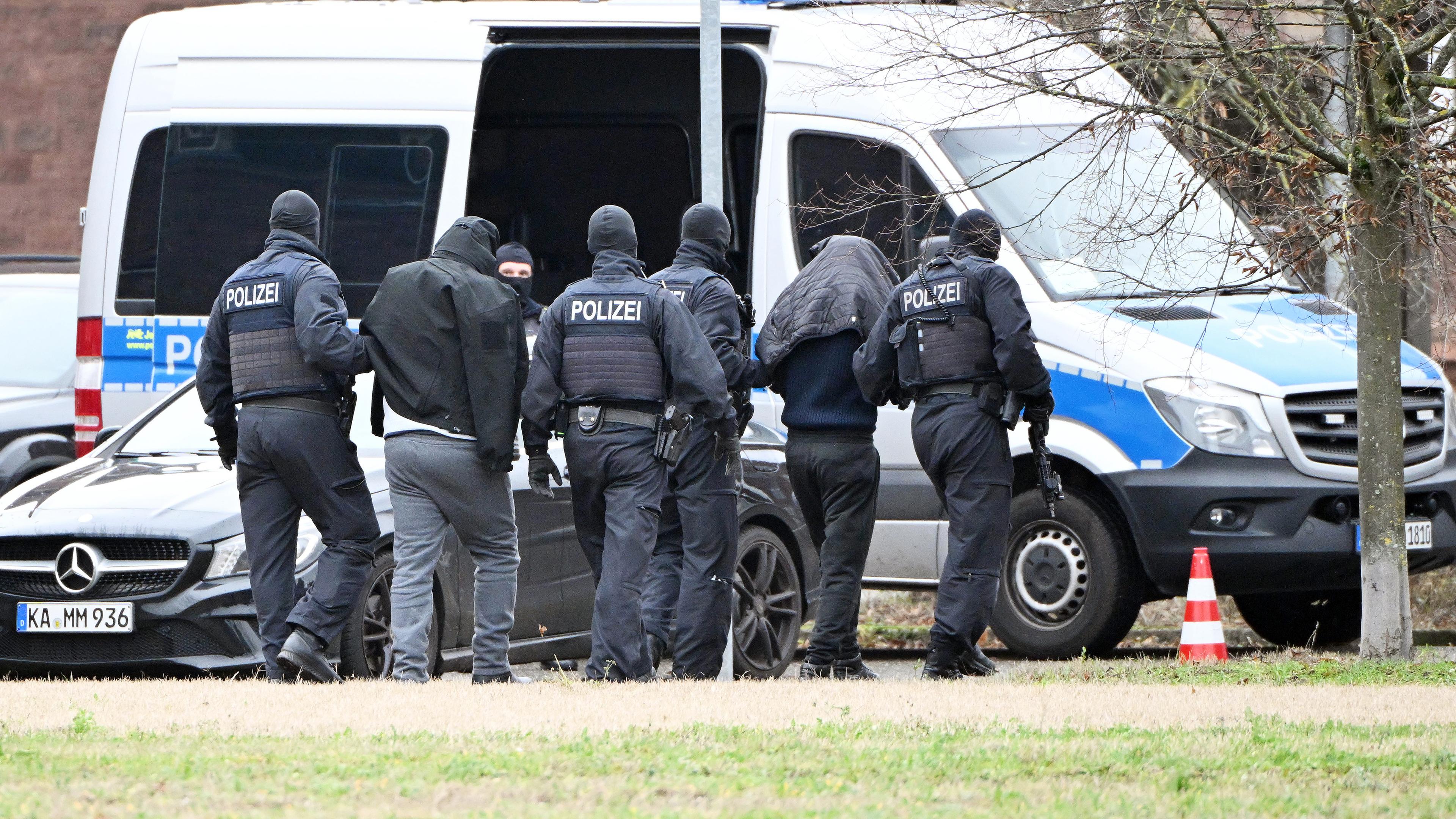 Baden-Württemberg, Karlsruhe: Zwei Personen werden von Polizisten bei einem Hubschrauberlandeplatz von einem Hubschrauber zu einem Auto geführt.