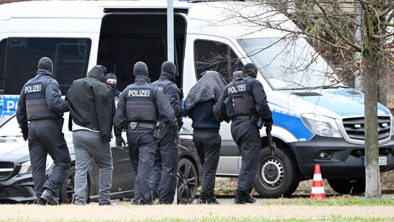 Baden-Württemberg, Karlsruhe: Zwei Personen werden von Polizisten bei einem Hubschrauberlandeplatz von einem Hubschrauber zu einem Auto geführt.