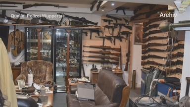 Auf dem Bild ist zu sehen: In einem möblierten Zimmer hängen zahlreiche Schusswaffen dicht nebeneinander an den Wänden.