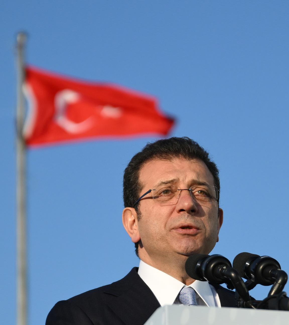 Ekrem Imamoglu hält eine Rede während die türkische Flagge im Hintergrund zu sehen ist.