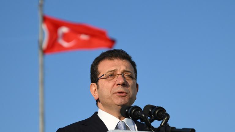 Ekrem Imamoglu hält eine Rede während die türkische Flagge im Hintergrund zu sehen ist.