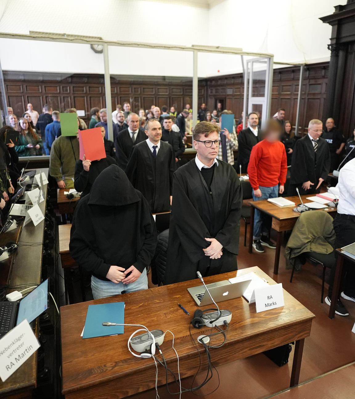 Die Angeklagten stehen im Sitzungssaal im Strafjustizgebäude zu Beginn des Prozesses
