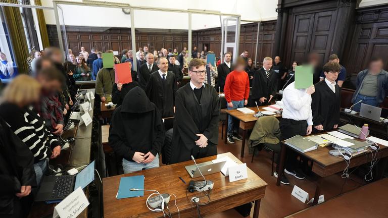 Die Angeklagten stehen im Sitzungssaal im Strafjustizgebäude zu Beginn des Prozesses