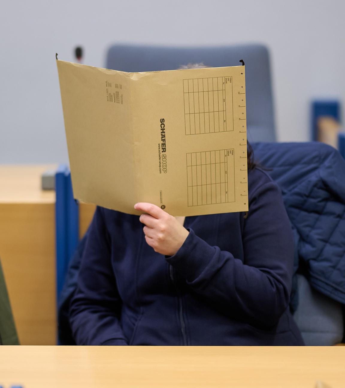 Eine angeklagte Mutter verbirgt im Gerichtssaal ihr Gesicht hinter einer Akte. 