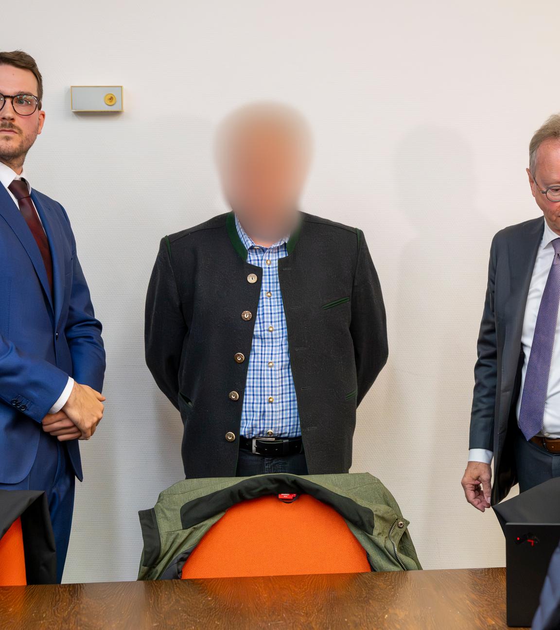 Ein beschuldigter Bahnmitarbeiter (M) steht vor Prozessbeginn um das tödliches Zugunglück in Garmisch-Partenkirchen vom 3. Juni 2022 zwischen Anwälten im Gerichtssaal