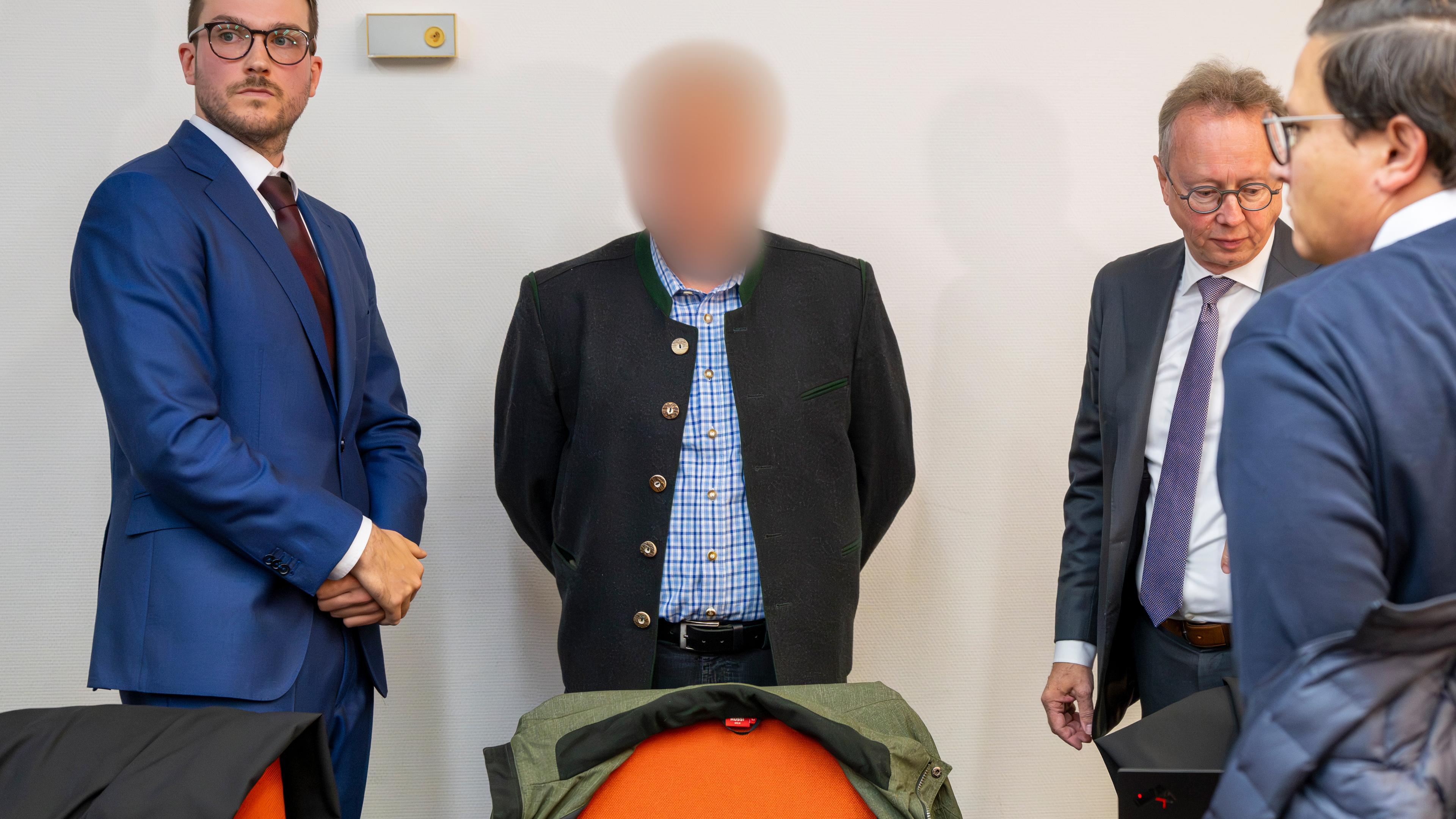 Ein beschuldigter Bahnmitarbeiter (M) steht vor Prozessbeginn um das tödliches Zugunglück in Garmisch-Partenkirchen vom 3. Juni 2022 zwischen Anwälten im Gerichtssaal