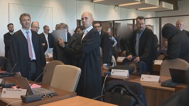 Gerichtssaal mit vielen Menschen Anwälte, in Robe und der Angeklage der sein Gesicht mit einer Mappe bedeckt.