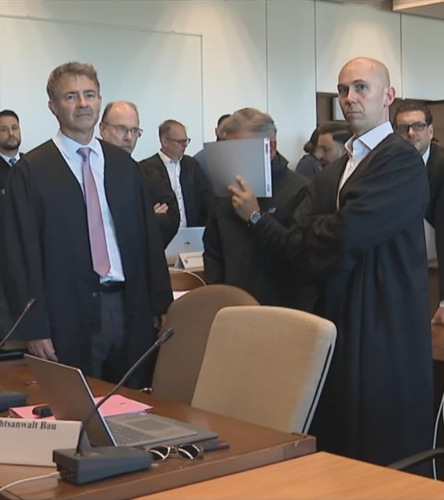 Gerichtssaal mit vielen Menschen Anwälte, in Robe und der Angeklage der sein Gesicht mit einer Mappe bedeckt.