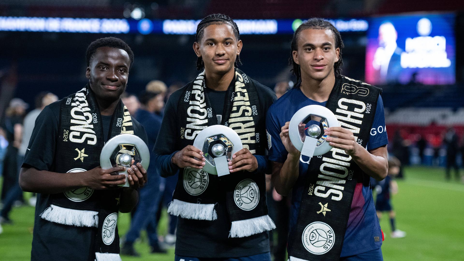 Die PSG-Spieler Yoram Zague, Senny Mayulu und Ethan Mbappe (von links) zeigen nach dem Gewinn der französischen Meisterschaft eine Trophäe am 12. Mai 2024