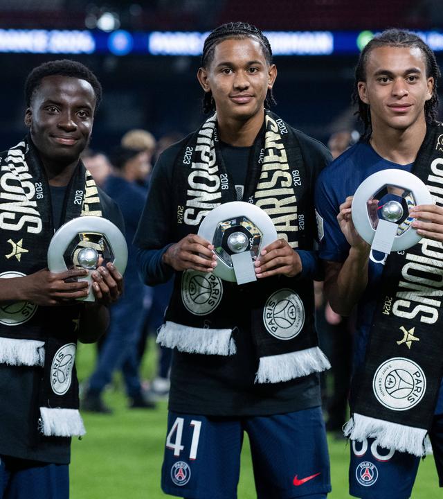 Die PSG-Spieler Yoram Zague, Senny Mayulu und Ethan Mbappe (von links) zeigen nach dem Gewinn der französischen Meisterschaft eine Trophäe am 12. Mai 2024