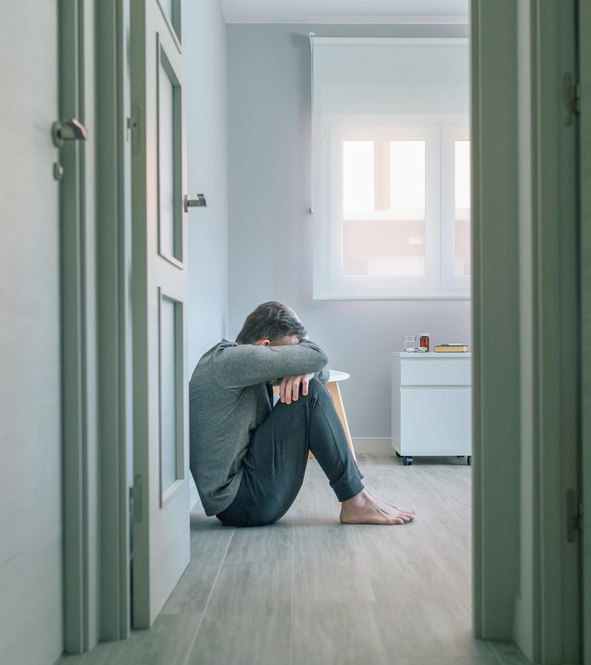 Unerkennbarer Mann mit psychischer Störung weint auf dem Fußboden eines psychiatrischen Zentrums
