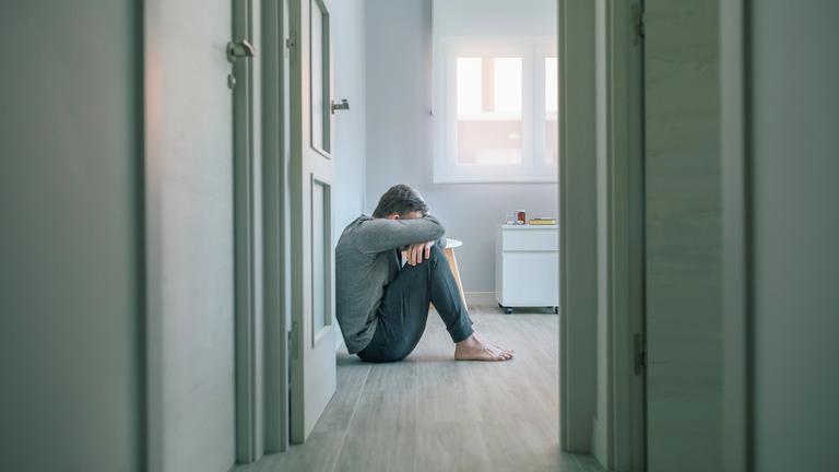 Unerkennbarer Mann mit psychischer Störung weint auf dem Fußboden eines psychiatrischen Zentrums