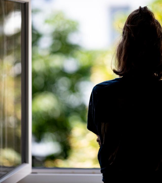 Berlin: Eine Frau steht in ihrer Wohnung an einem Fenster.