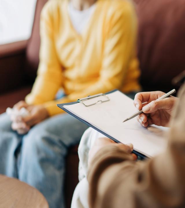 Nahaufnahme der Hände einer Psychologin, die sich in Notizen über ihre Patientin macht.