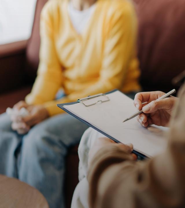 Nahaufnahme der Hände einer Psychologin, die sich in Notizen über ihre Patientin macht.