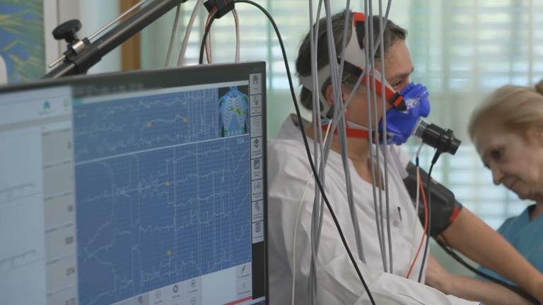 Eine Frau während einer Spiroergometrie auf einem Ergometer mit einer Sauerstoffmaske.