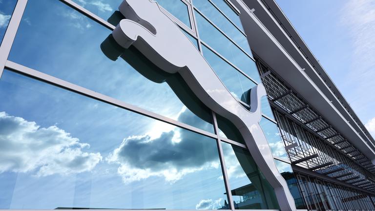 Bayern, Herzogenaurach: Wolken spiegeln sich im Fenster hinter einem Puma-Logo am Firmensitz des Sportartikelherstellers
