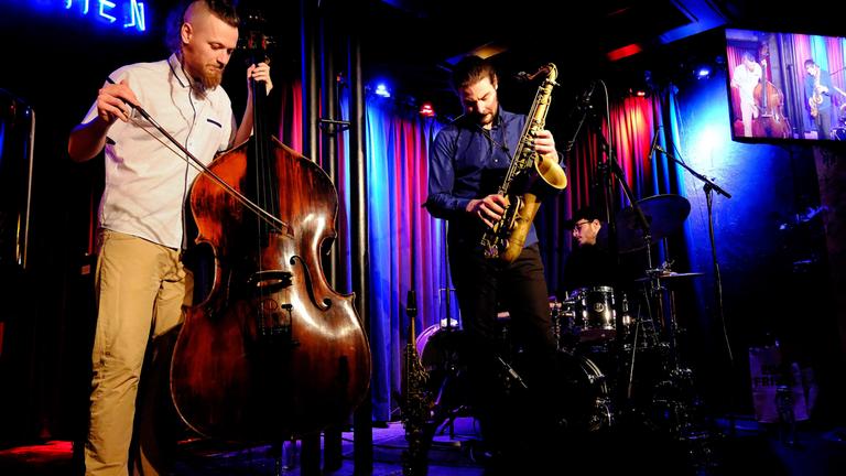 Zwei Musiker mit Kontrabass und Klarinette spielen auf einer blau und lila angeleuchteten Bühne.