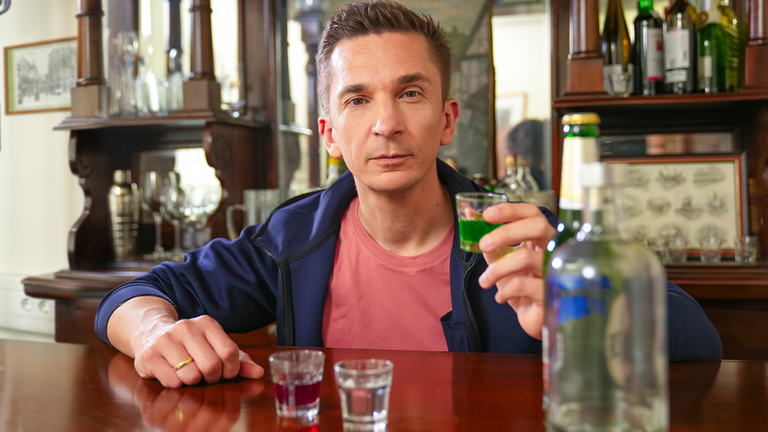 Eric sitzt an einer Bar und hält ein Glas mit Alkohol gefüllt in der Hand. Vor ihm stehen weitere Gläser und Flaschen.