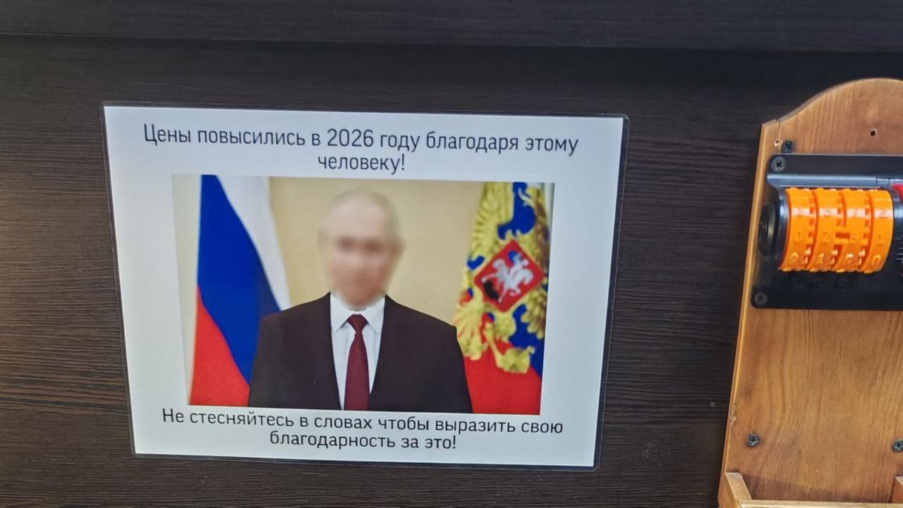 Ein Plakat ist an einer Regalwand in einem Supermarkt angebracht. Zu sehen ist ein Bild mit Vladimir Putin und kyrillische Schrift.