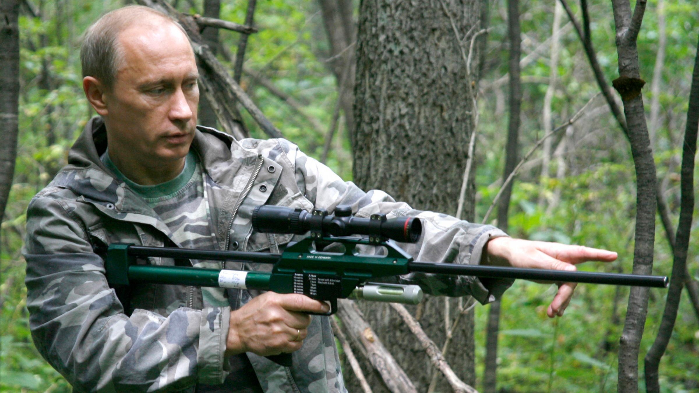 Der russische Präsident Wladimir Putin steht mit einem Betäubungsgewehr im Wald.