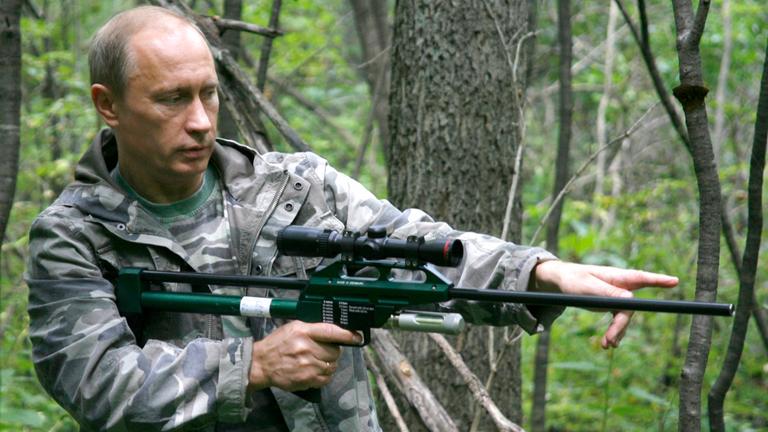 Der russische Präsident Wladimir Putin steht mit einem Betäubungsgewehr im Wald.