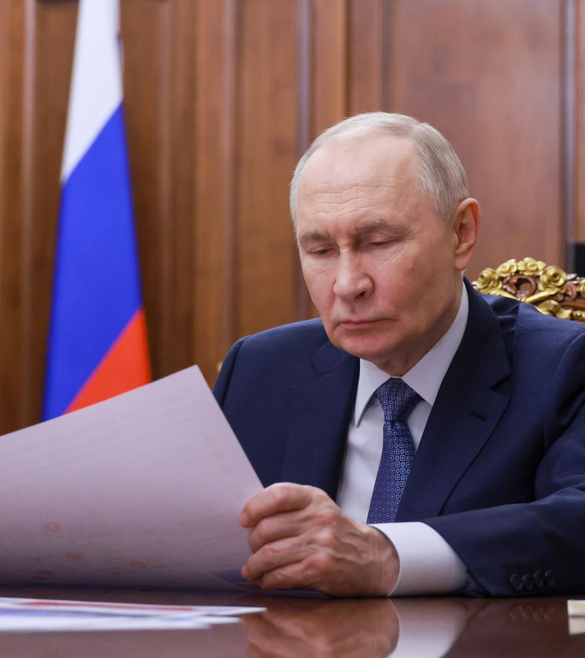 Vladimir Putin sitzt im Anzug an einem Holztisch und schaut auf Papiere.