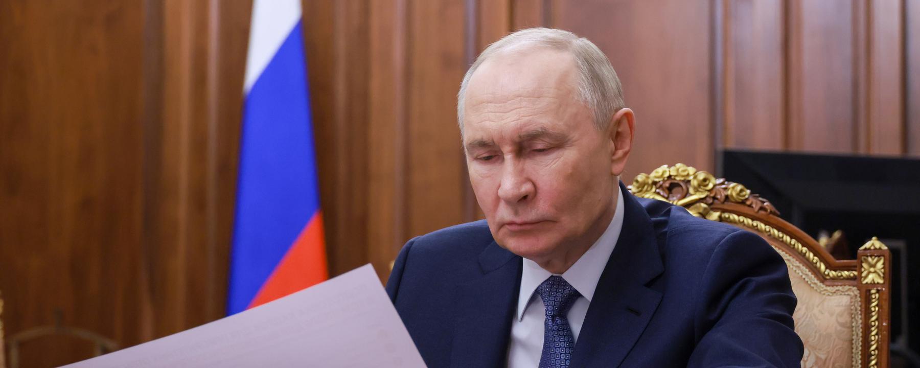 Vladimir Putin sitzt im Anzug an einem Holztisch und schaut auf Papiere.