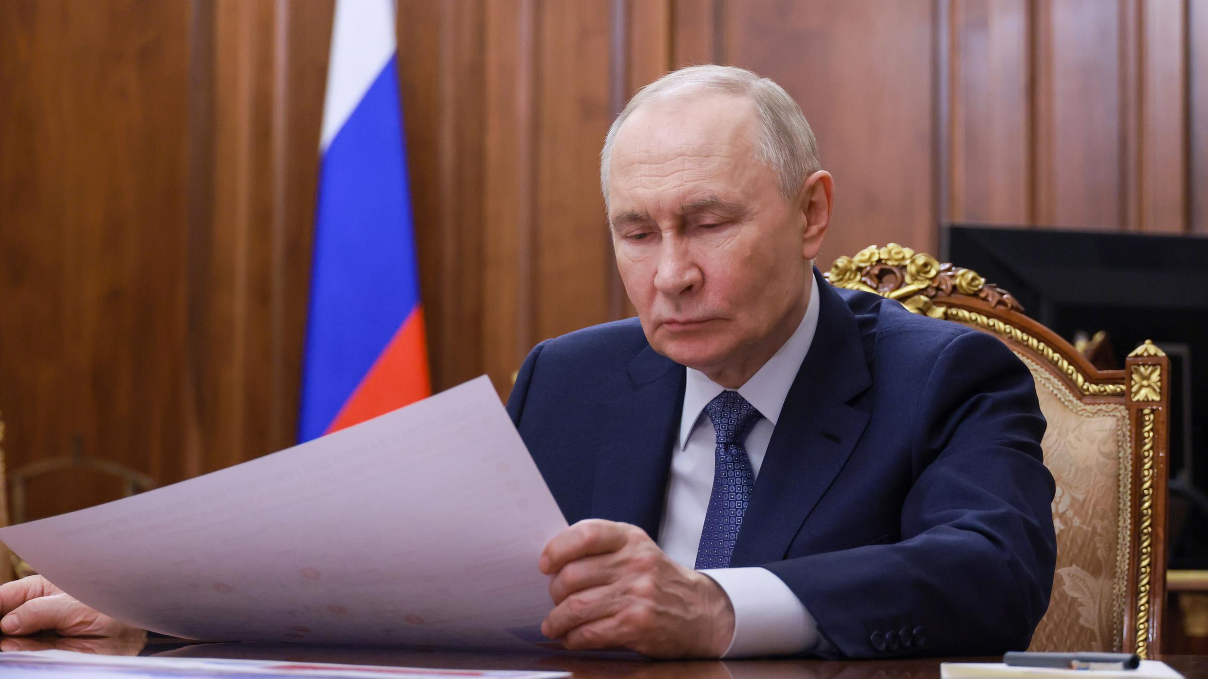 Vladimir Putin sitzt im Anzug an einem Holztisch und schaut auf Papiere.