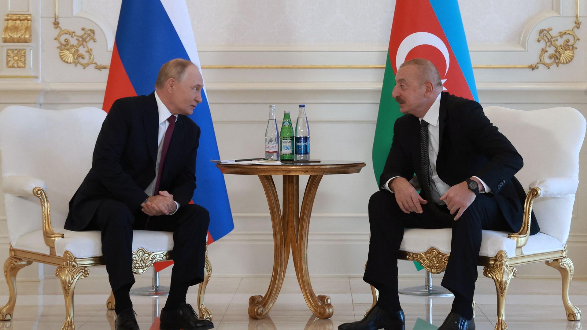 Aserbaidschans Präsident Ilham Alijev (rechts) und Russlands Präsident Wladimir Putin (links) sitzen vor ihren jeweiligen Nationalflaggen und sprechen miteinander.