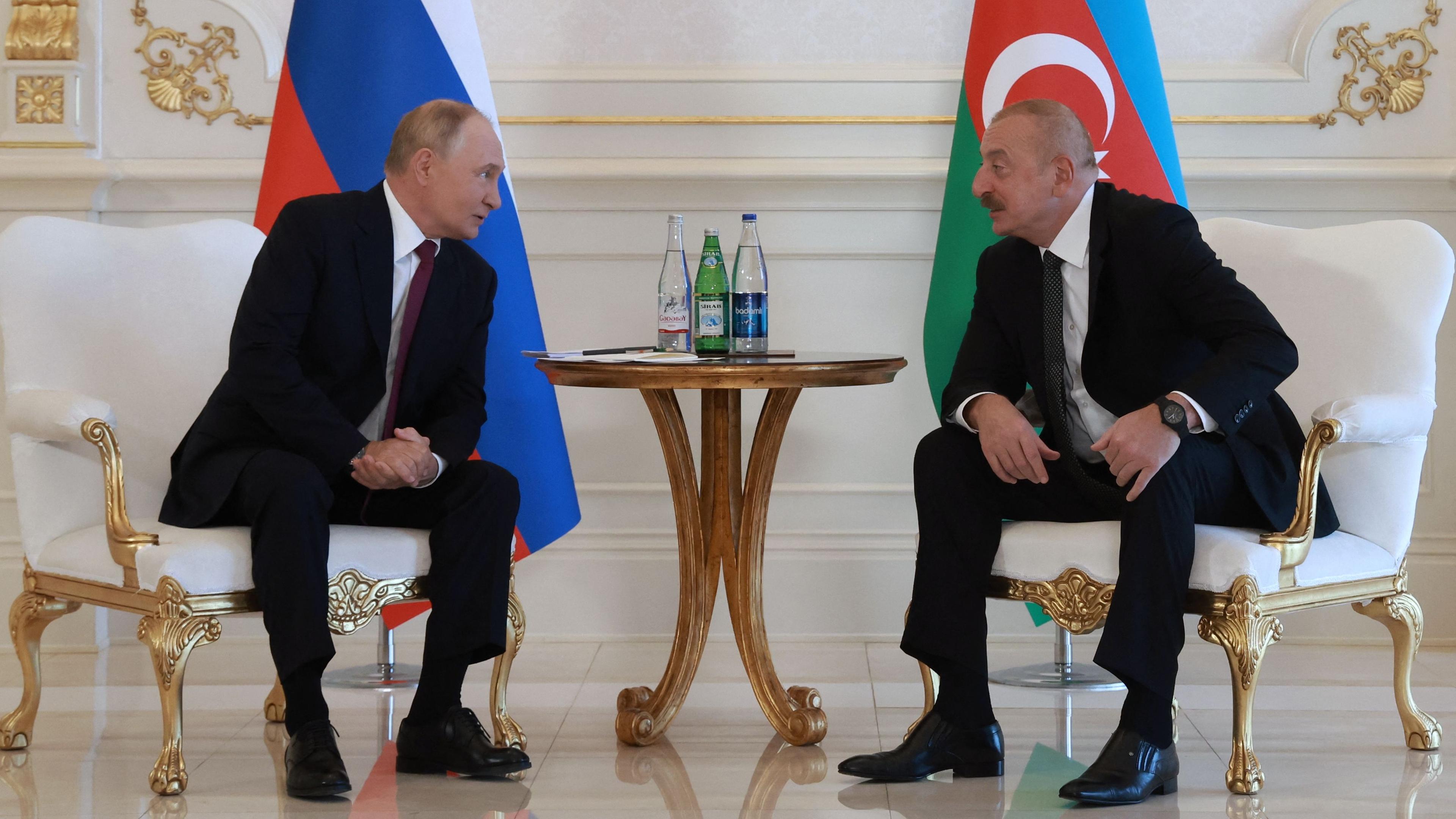 Aserbaidschans Präsident Ilham Alijev (rechts) und Russlands Präsident Wladimir Putin (links) sitzen vor ihren jeweiligen Nationalflaggen und sprechen miteinander.