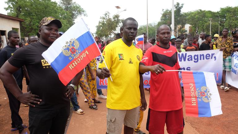 Eine Gruppe von Männern steht auf einer Straße. Zwei von ihnen halten Russland-Flaggen in den Händen.
