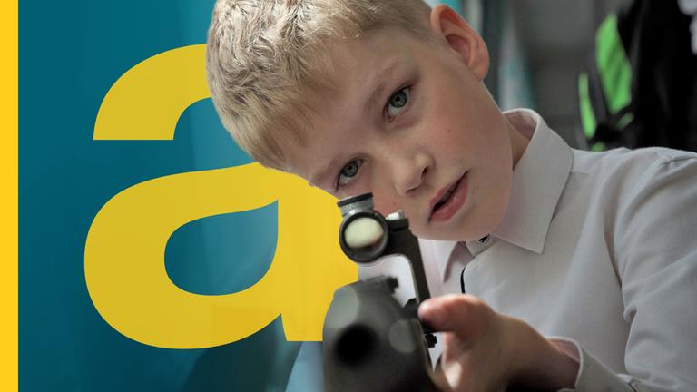 Russischer Junge mit blonden Haaren zielt mit Gewehr Richtung Kamera