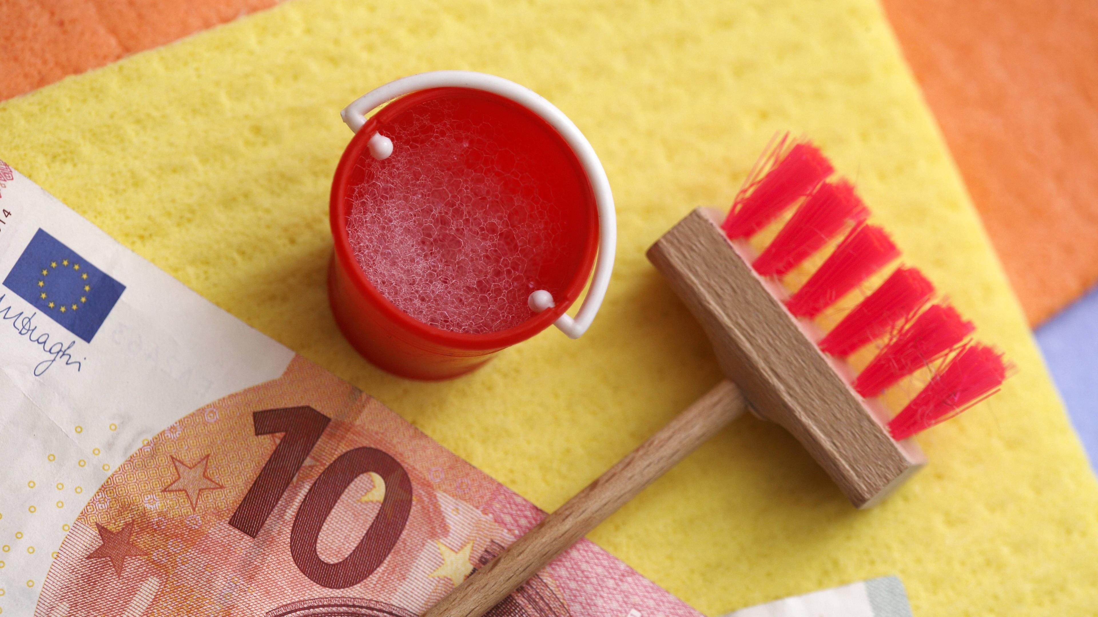 10-Euro-Schein, Haushaltsschwamm, Putzeimer und Besen