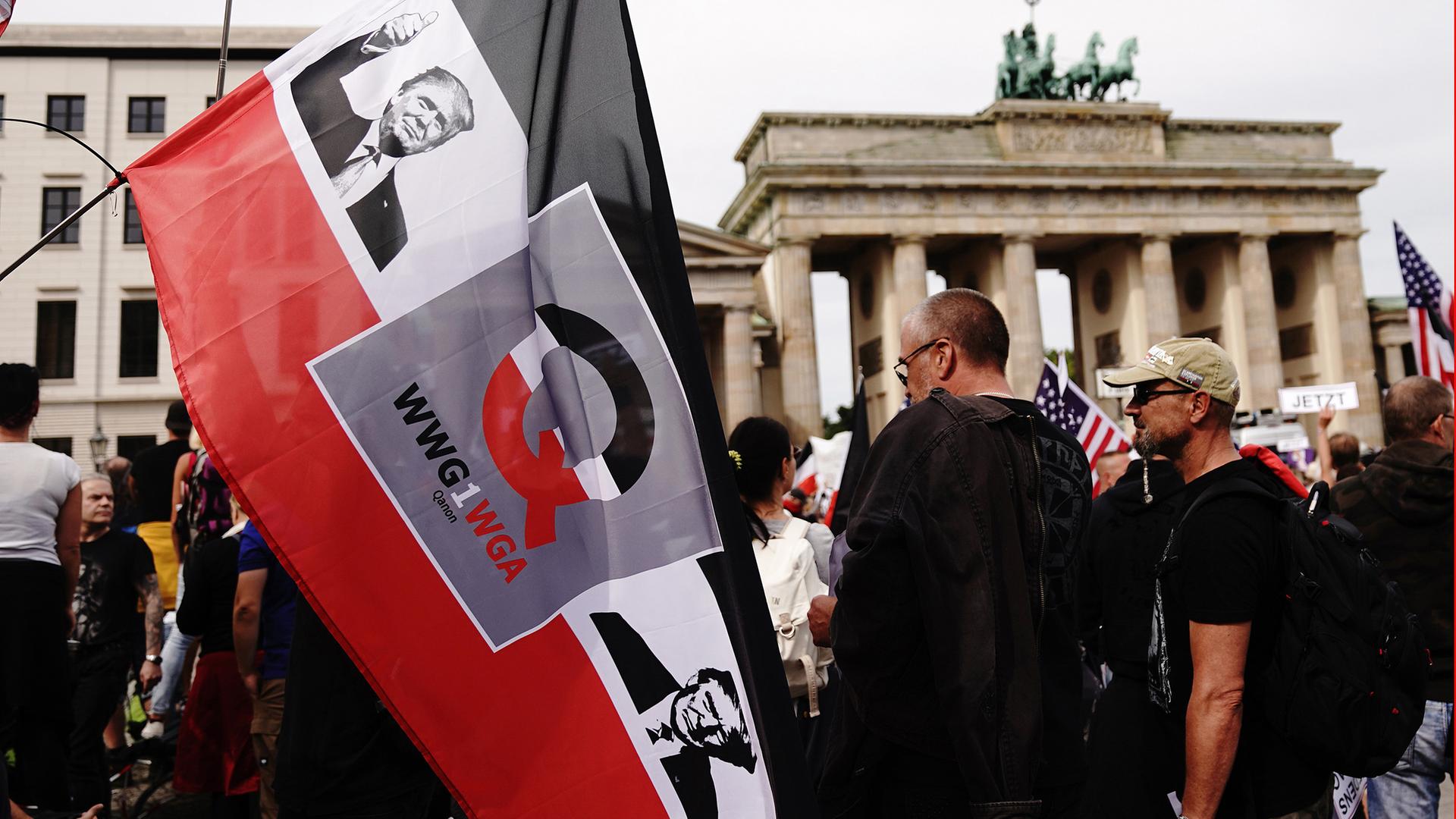 Archiv, Berlin: Auf einer schwarzweissroten Fahne, die ein Teilnehmer vor dem Brandenburger Tor hält, sind ein Bild von US Präsident Trump, der Buchstabe "Q" sowie der Schriftzug "WWG1WGA" (where we go one, we go all) aufgedruckt.
