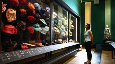Ein Mitarbeiter neben einer Ausstellung verschiedener Hüte der Ausstellung „Queen Elizabeth II: Her Life in Style“ in der King’s Gallery im Buckingham Palace in London.