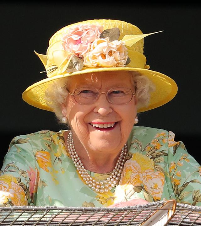 Queen Elizabeth trägt einen gelben Hut mit Blumen und grinst in die Kamera