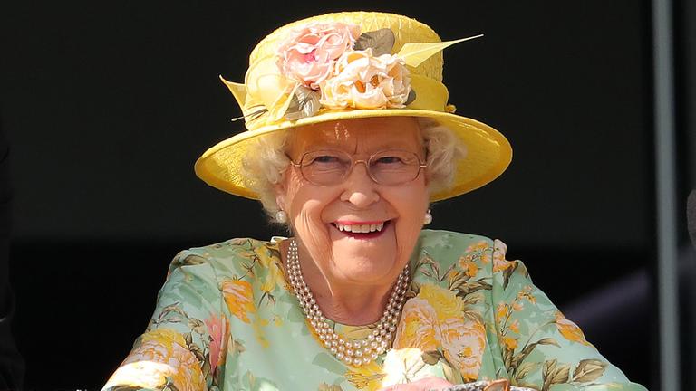 Queen Elizabeth trägt einen gelben Hut mit Blumen und grinst in die Kamera